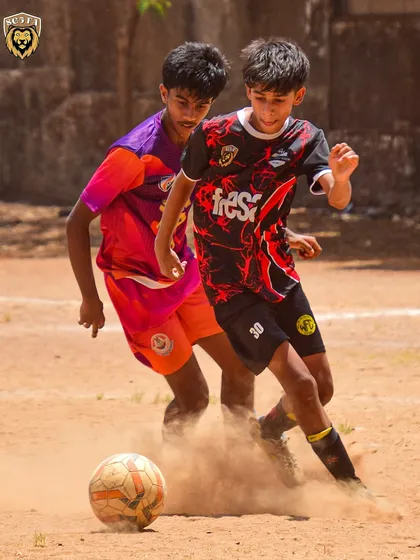 A young player skillfully dribbling past an opponent in a cloud of dust, showing pure determination.