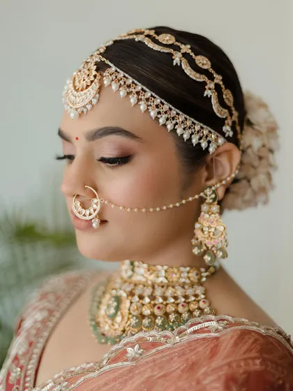 A study in bridal beauty. This profile shot showcases the complete hair, makeup, and jewelry styling, from the intricate matha patti to the layered choker, all chosen to create a look of timeless elegance.