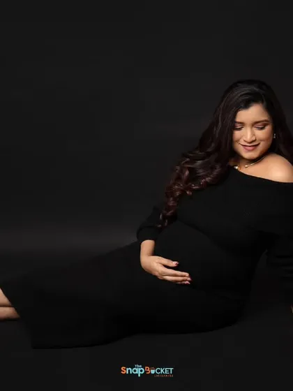 A simple, elegant portrait of the mom-to-be in a classic black off-the-shoulder dress. The dark backdrop and focused lighting create a moody and sophisticated feel.