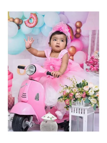 Waving to the camera, this little girl is ready to ride off on her pink scooter. The pastel balloons and floral arrangements create a beautiful and sweet setting for her photoshoot.