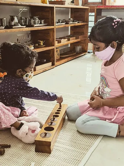 One of the most valuable aspects of our classroom is the mixed-age group. Here, a four-year-old child naturally takes on the role of a mentor, helping a two-year-old with the knobbed cylinders. This interaction builds empathy, leadership, and a true sense of community.