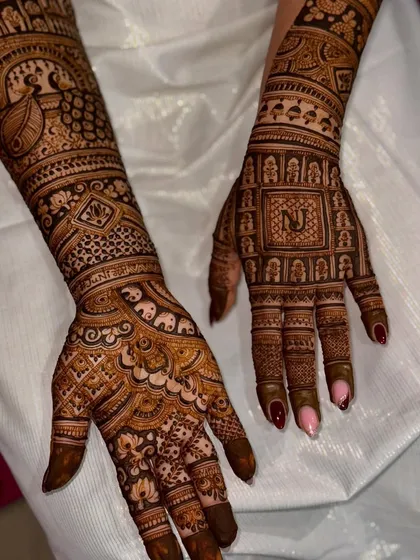 Another angle of a personalized bridal design, showing the initial 'N' and the detailed peacock. The consistency and richness of the henna paste are visible throughout.