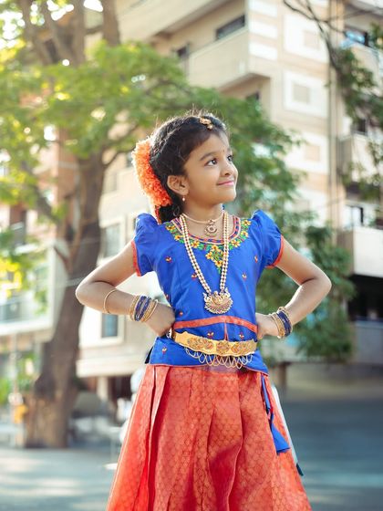 Posing with pride in her traditional blue and red outfit. This outdoor shot captures the vibrant colors of her dress against a natural backdrop.