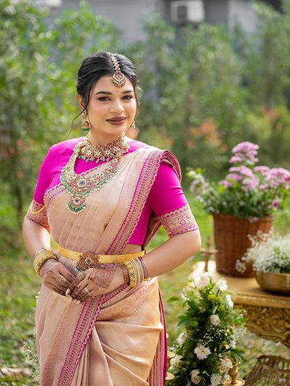 A bride posing in a garden, her cream and pink saree looking fresh and beautiful. The gold belt adds a touch of modern glamour.