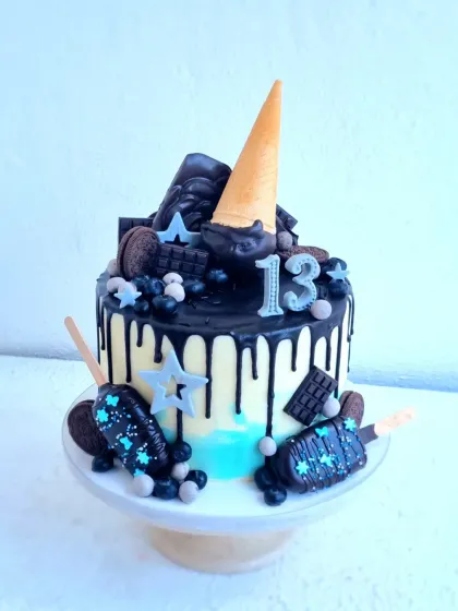 A fun drip cake for a 13th birthday. This design includes a dark chocolate drip, chocolate-dipped cakesicles, and various chocolate candies.