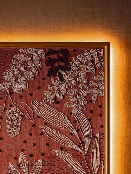 The corner detail of our framed and backlit embroidered wallpaper. The warm light catches the intricate threadwork, highlighting the craftsmanship and turning the wall into a focal point that is both refined and rooted in craft.