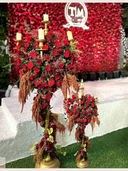 A close-up of a candelabra-style floral arrangement against a wall of red roses. This detail adds a touch of classic romance and luxury to a vibrant and bold event theme.