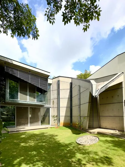The 'House of Stories' seen from its garden, seven years after completion. We design buildings to grow with their inhabitants and settle into their landscapes. The relationship between the concrete forms, the greenery, and the sky is a story that unfolds over time.