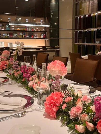 A close-up of the elegant dinner table setting. The long floral runner, composed of various shades of pink and lilac, provided a beautiful and luxurious element that elevated the entire dining experience.