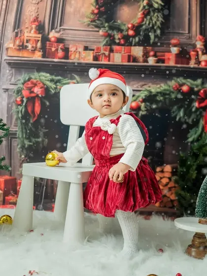A toddler using a small chair to practice standing, interacting with the props in the Christmas scene.