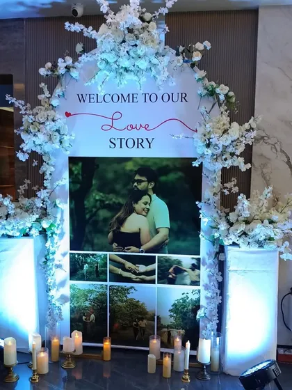 A personalized entrance we designed for a pre-wedding celebration. It features a photo collage of the couple's journey, framed by a beautiful white floral arch and warm candle lighting to welcome guests.