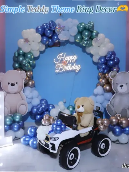 A detailed look at the simple and sweet teddy bear theme. The setup includes a circular balloon arch in shades of blue and brown, a "Happy Birthday" neon sign, and adorable teddy bear props.