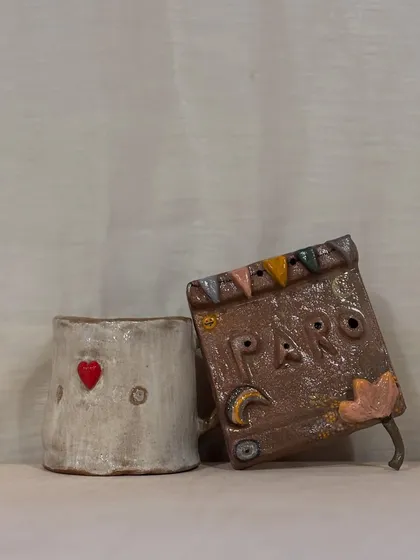 A student's two finished pieces: a heart-stamped mug and a whimsical hanging book decor.
