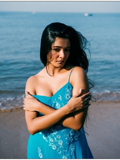 A full-body shot on the beach, with the ocean creating a serene and beautiful backdrop. The natural light and wind create a sense of movement in her hair and dress. The model's pose feels vulnerable yet strong, telling a quiet story.