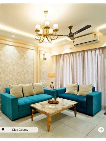 A vibrant living room with a teal sofa and a classic chandelier. The design uses wallpaper and simple wall molding to add character without overwhelming the space.