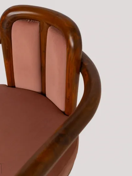 A detail shot of the 'Svelte' chair, showing the beautiful curve of the bent teakwood armrest and the soft mauve fabric.