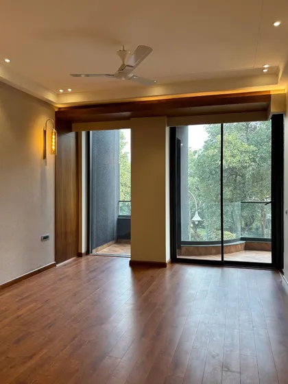 An unfurnished bedroom space with warm wooden flooring and large windows opening to a balcony, showcasing the excellent natural light and spatial potential.