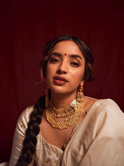 A close-up portrait with a direct, captivating gaze. The simple composition against a rich red backdrop puts the focus entirely on the model's expression and the stunning jewelry.