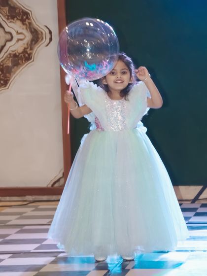 The birthday girl in a beautiful gown, happily holding a large clear balloon on the dance floor.