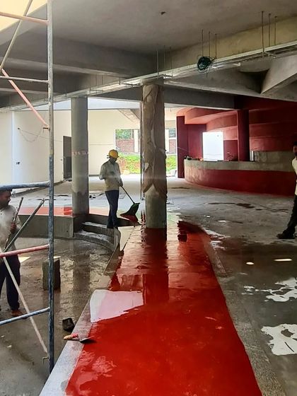 Workers spreading and polishing the red oxide mixture on the floor of the TAPMI Centre, a physically demanding process that results in a seamless, vibrant surface.