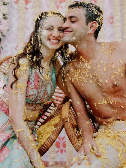 A joyful and messy Haldi portrait. The couple's happy, turmeric-covered faces show the fun and love shared during this pre-wedding ritual.