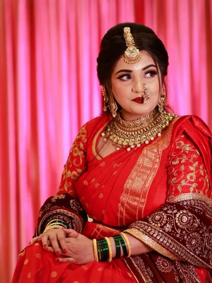An elegant engagement look for a Maharashtrian bride. The red saree and gold jewelry are complemented by a classic makeup look with a bold red lip.