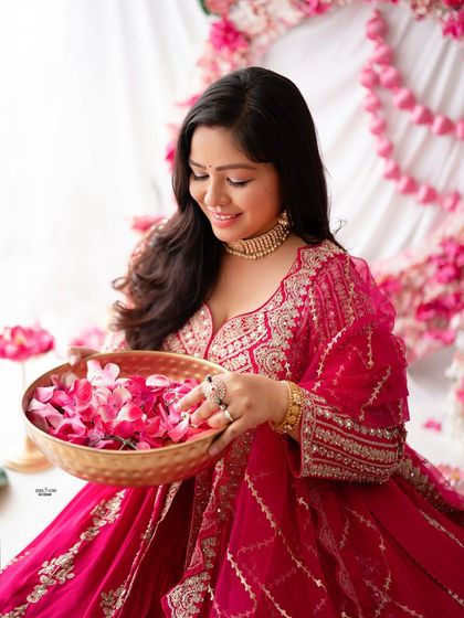 A beautiful portrait of a mother-to-be in a traditional pink outfit, holding a bowl of flower petals. The setup is rich with color and cultural aesthetics.