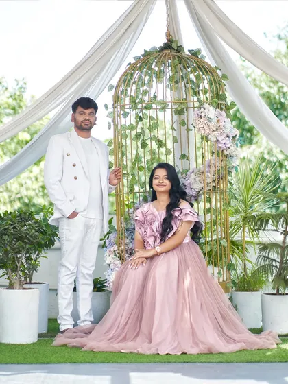 A full-length portrait of the couple in our studio's garden setup. The groom's all-white outfit is a perfect match for the bride's soft pink gown.