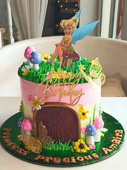 A whimsical Tinker Bell cake set in a fairy garden, complete with a wood-grain door, colorful mushrooms, and delicate butterflies for a magical birthday.