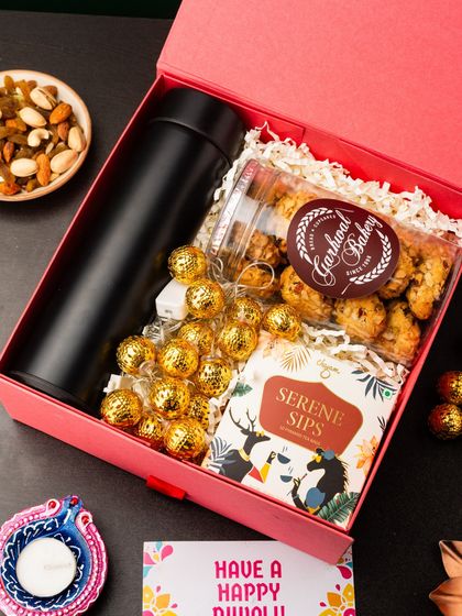 A perfect gift for a valued client or team lead, this hamper includes a black thermos flask for their daily commute. It's paired with premium cookies, Ferrero Rocher chocolates, and a box of serene sips tea, all presented in a festive pink box.