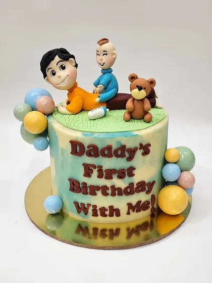 A cake celebrating "Daddy's First Birthday With Me," topped with cute figurines of a father and his baby.