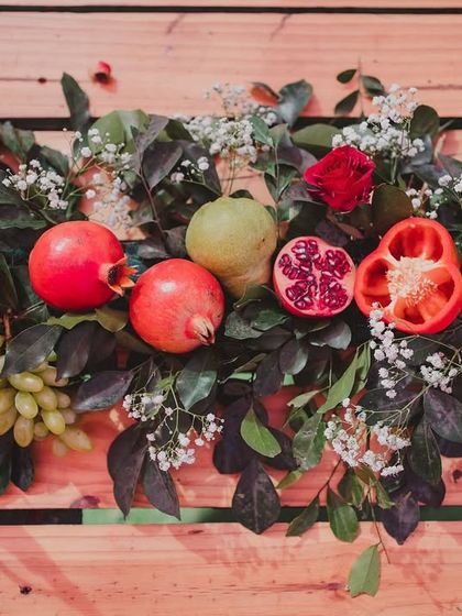 A beautiful arrangement of pomegranates, bell peppers, and grapes with baby's breath and roses, showcasing the artful use of edible elements in the decor.