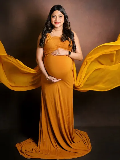 A classic maternity pose with a fabric toss for added movement and drama. The mom-to-be looks radiant in this mustard yellow gown against a simple, dark backdrop that makes the color pop.