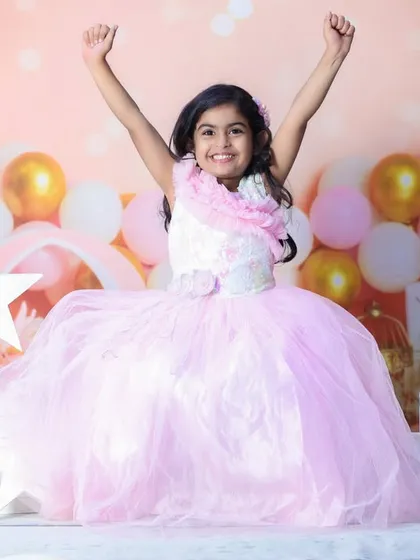 Pure joy! This little girl in a beautiful pink dress is having the time of her life during her birthday photoshoot. The sparkly balloon background adds to the celebration.