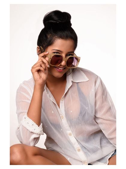 A casual and fun studio portrait. The oversized sunglasses and sheer shirt create a relaxed, summery feel, ideal for a lifestyle or accessory brand.