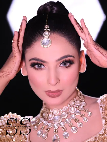 This shot highlights the neat bridal bun and the placement of the maang tikka. Notice how the model's hands with henna frame her face, adding to the traditional bridal aesthetic.