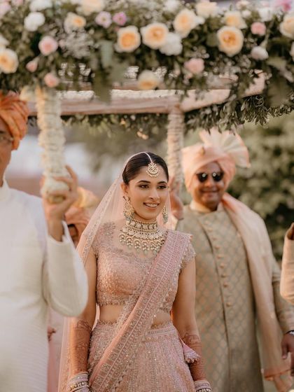 The bride's grand entrance under a floral canopy. Her soft makeup and pastel outfit look ethereal.
