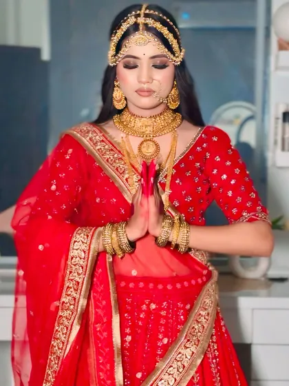 A bride in a 'Padmavati' inspired red lehenga, posing with hands joined in a traditional gesture. The heavy gold jewellery and intricate outfit details are on full display.