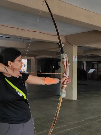 An adult archer practices her form, drawing the bowstring back smoothly. We provide all necessary safety gear, including the arm guard seen here, for a comfortable shooting experience.