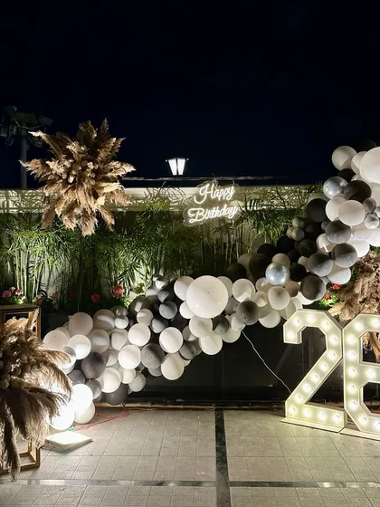 A chic and modern setup for a 26th birthday. We created a beautiful photo backdrop with a black and white balloon arch, pampas grass arrangements, a neon sign, and marquee numbers.
