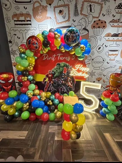 This superhero-themed party for a 5th birthday is packed with action. It features a balloon arch with Hulk, Spiderman, and Iron Man, a neon sign, and a marquee number '5'.