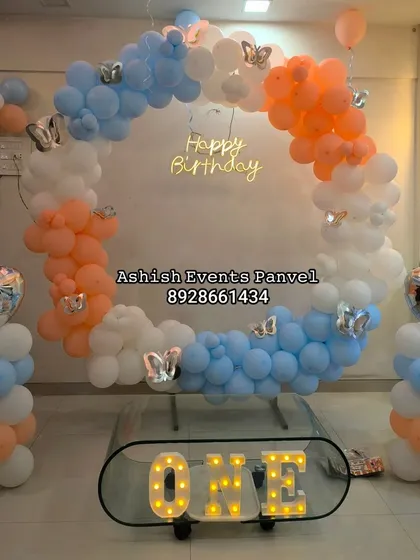 A modern and elegant ring backdrop for a first birthday. The pastel blue, orange, and white balloons, accented with butterfly details and a neon sign, create a sophisticated and trendy look for milestone celebrations.