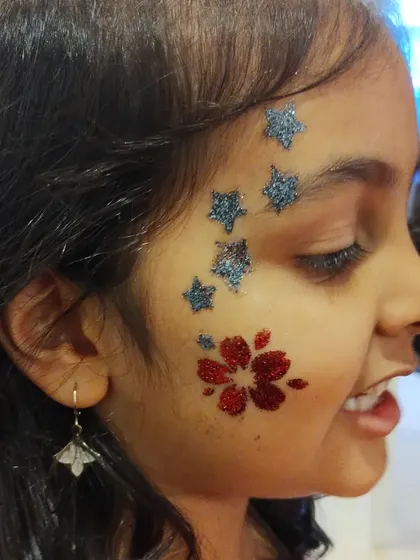 I love combining different elements to create a unique look. Here, I've paired a sparkling red flower on the cheek with a trail of blue glitter stars for a fun and whimsical face art design.