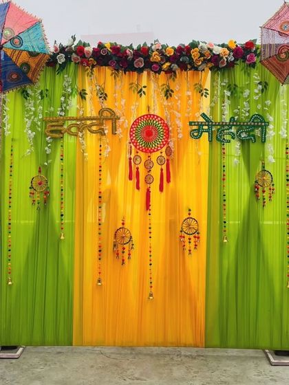 A fresh and airy outdoor backdrop for a Haldi Mehandi function. The light green and yellow drapes are decorated with dreamcatchers, bells, and hanging umbrellas.