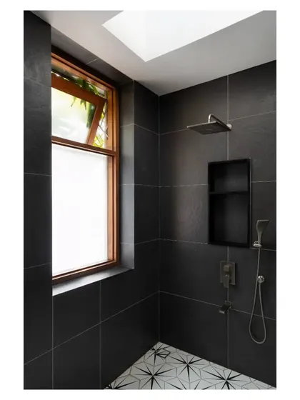 A skylight illuminates this minimalist shower, clad in dark stone tiles that contrast with the patterned floor, creating a dramatic and private space.