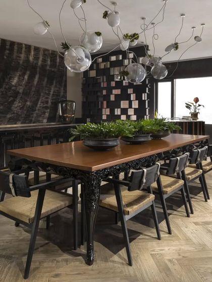 A full view of the dining setup in the Caitriona apartment. The combination of the heavy, sculptural 'Hybrid Table' with the lighter 'Campaigning Chairs' and the ethereal Bocci lights creates a perfectly balanced and dynamic composition.