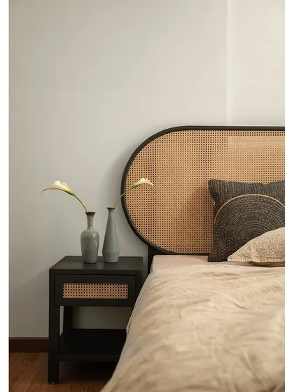 A close-up of the bedside details in the guest bedroom. The combination of the rattan headboard, the simple black side table, and the delicate flowers creates a feeling of timeless charm.