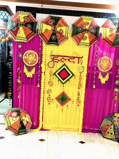 A vibrant and traditional Haldi ceremony backdrop, using bright yellow and magenta drapes, marigold garlands, and decorative Rajasthani umbrellas for a festive look.