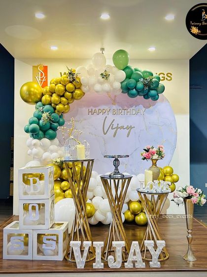 An elegant birthday backdrop in green, white, and gold. The marble-print circular backdrop, twisted-leg pedestals, and marquee letters create a sophisticated and luxurious feel.