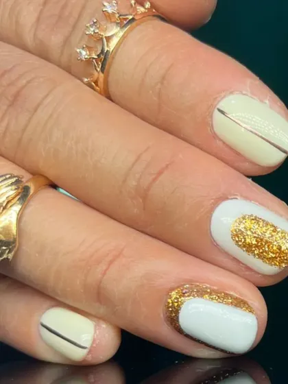 A close-up of the elegant off-white and gold glitter manicure.
